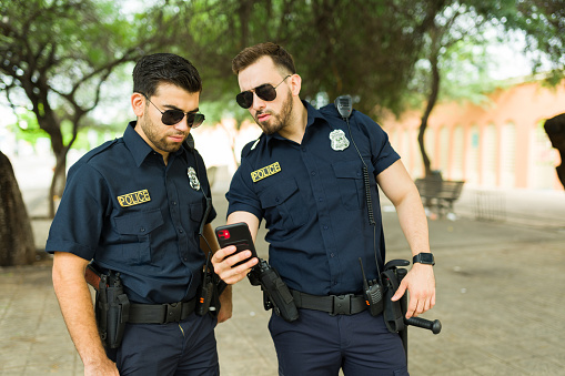 Police agents with sunglasses looking at a text message or a crime report on the smartphone while chasing a criminal with GPS