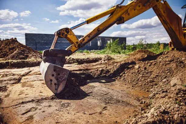 Excavator working at house construction site - digging foundations for modern house. Beginning of house building. Earth moving and foundation preparation.