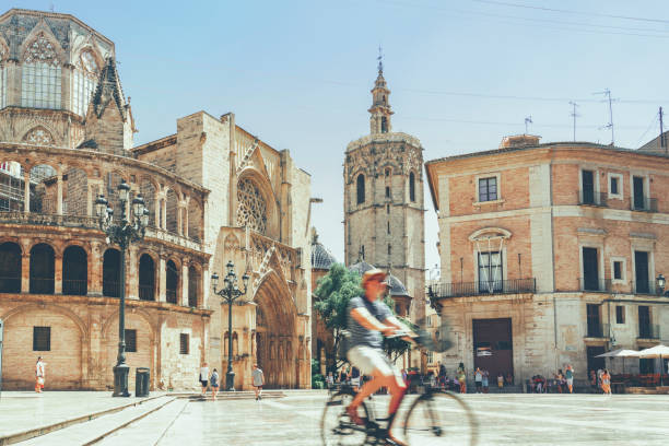 tourist ridding bicycle through plaza mare de deu with valencia cathedral in background spain - valencia cathedral imagens e fotografias de stock