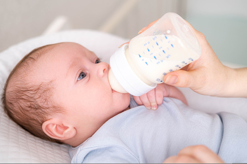 loving mother feeding her little boy child with milk baby bottle at home, portrait infant Baby eating, drinking powdered milk