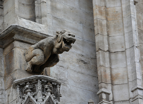 Monstrous statue with almost human features called gargoyle on the facade of the historic building