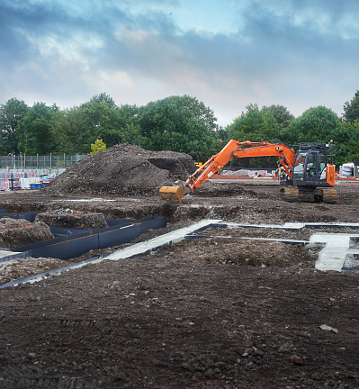 An excavator sits on the site of a new housing estate among freshly dug and laid foundations