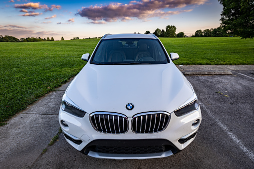 Lexington, Kentucky USA - Sep 7 2022: Frontal view of white 2017 BMW X1 on a parking spot in front of a lawn in Jacobson park during sunset.