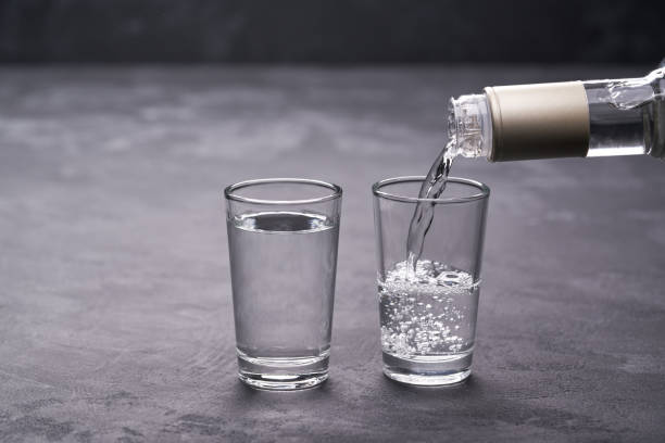 Vodka from the bottle is poured into a glass on a black background, selective focus stock photo