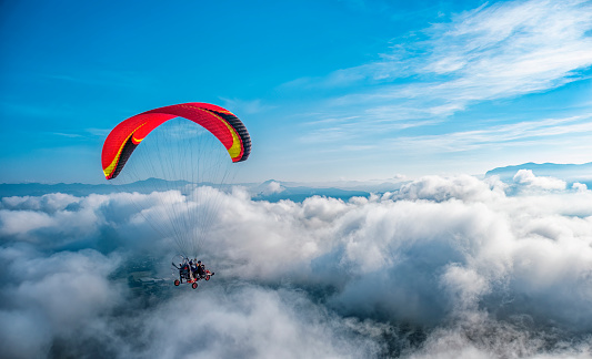 Red paramotor flying in the blue sky with puffy white cloud. Extreme activity concept.