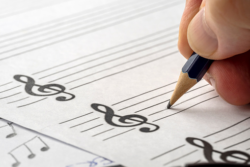 MUSIC COMPOSER WRITING NOTES WITH PENCIL ON THE STAVE. MUSIC SHEET FOR SONG WRITER . CLOSE UP. COPY SPACE.