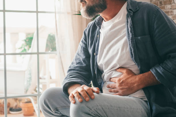 homme souffrant de douleurs sévères à l’estomac assis à la maison. main d’un gars mature tenant l’abdomen souffrant de douleurs, de diarrhée ou de problèmes digestifs. homme de race blanche appuyant sur le ventre sur une sensation douloureuse - uncomfortable photos et images de collection