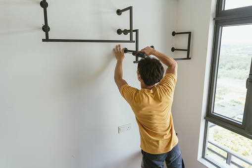Home Ownership - An Asian Chinese man installing a rack fixture to the wall