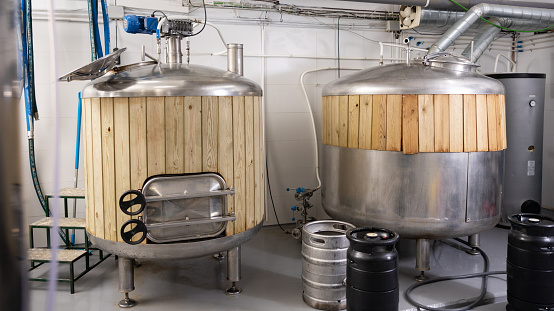 Interior of small private brewery with steel tanks trimmed with wooden planks for beer fermentation and kegs for storaging