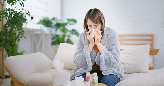 asian woman having running nose covering in the blanket feeling uncomfortable at home