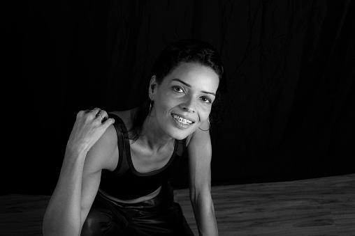 Studio Portrait in black and white of young woman in black t-shirt smiling at camera against black studio background. Salvador, Brazil.