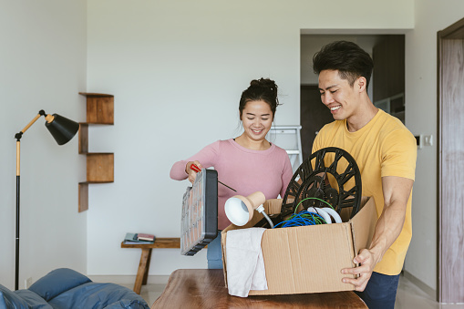 Home Ownership - Young adult Chinese couple bringing newly purchased home decor into their partially furnished new home