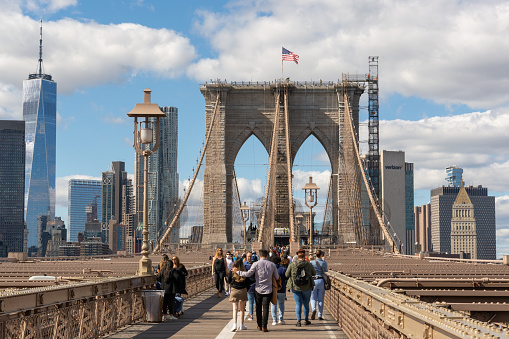 New York City, New York - October 1, 2021: Tourists and locals walking across the famous landmark Brooklyn Bridge which  connects the boroughs of Manhattan and Brooklyn with a view of lower Manhattan.