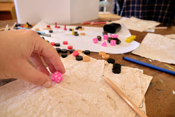 A players hand picks up a pink colored 20 sided dice (D20) during a role playing game A pink D20 (twenty sided dice) is about to rolled during a role playing game. A home made game map is on the table other pink and black dice of different sides, surrounded by other game pieces (some already in play, some ready to be used), as well as some sheets of paper, pens, pencils and an eraser developing 8 stock pictures, royalty-free photos & images