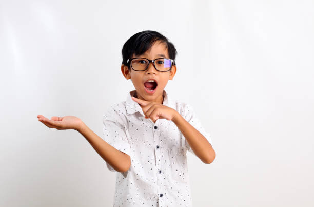 Surprised asian boy standing while presenting and pointing on empty space. Isolated on white