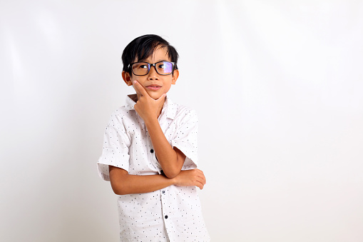 Thoughtful asian boy standing while touch his chin and looking side. Isolated on white background
