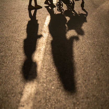 Photo of shadow of boy and mother pushing baby troller in sunset. Focus on shadows. Shot in outdoor during sunset. backlit effect is used.