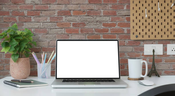 istock Front view laptop computer, coffee cup, stationary and houseplant on white table. Empty screen for your advertise text. 1423481159