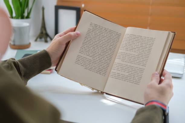 istock Over shoulder view, young man reading book in bright living room. 1423481912