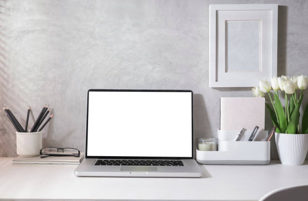 istock Bright modern home office with laptop, supplies and flower pot on white table. Empty screen for your advertise text. 1423484120