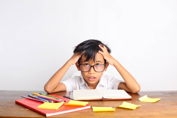 istock Confused asian schoolboy studying in classroom while holding his head. Isolated on white background 1423485418