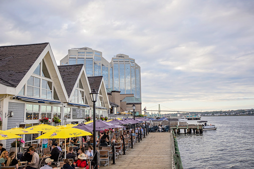 Halifax, Canada - August 28, 2022. People sit at tables by the water on a cloudy summer evening in downtown Halifax.