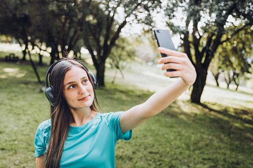Teenage girl, wearing turquoise t-shirt, taking a selfie with her smartphone in the public park