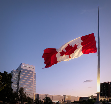 Windsor, Ontario, Canada - September 13, 2022:  The Canadian flag flying at half-mast overlooking the downtown Windsor skyline.