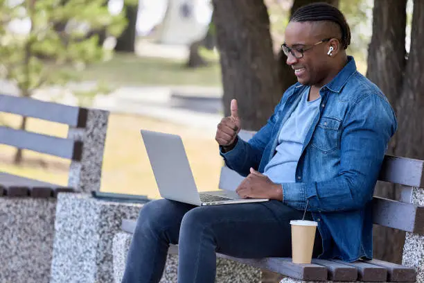 Photo of With hand gesture dark-skinned man shows subscribers in video chat great mood