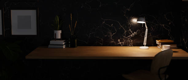istock Modern dark home workspace with copy space on wooden tabletop under warm light from table lamp 1423498285