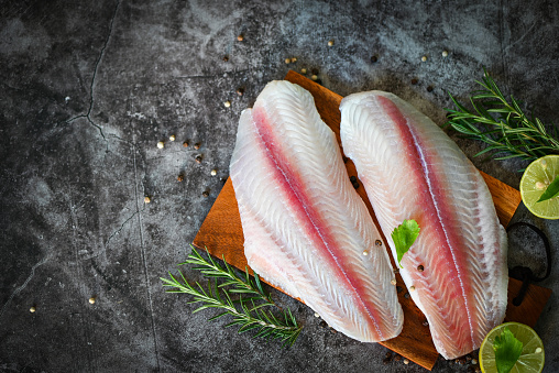 fish fillet on wooden board with ingredients for cooking, meat dolly fish tilapia striped catfish, fresh raw pangasius fish fillet with herb and spices black pepper lemon lime - top view