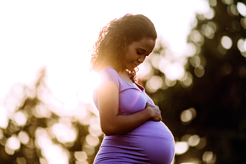 A mixed race young woman enjoys some relaxation time outdoors during the final weeks of her pregnancy, soaking in the summer sun and thinking of the days to come.  A healthy active lifestyle for her and her unborn baby.