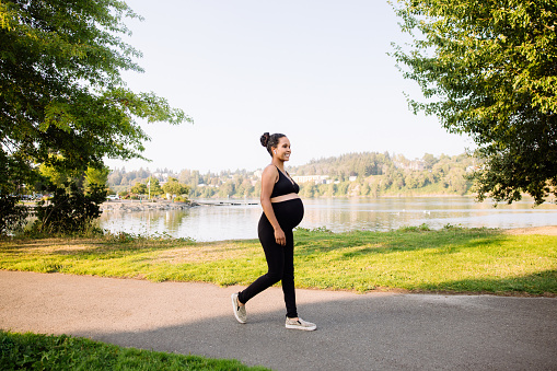 A mixed race young woman enjoys an exercise walk during the final weeks of her pregnancy, enjoying the summer sun and fresh air.  A healthy active lifestyle for her and her unborn baby.