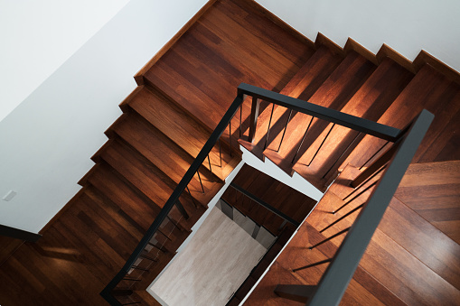 Modern solid dark brown wooden stairs in new house interior leading downwards with sunlight