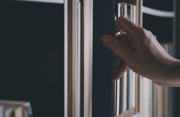 istock Hand looking for book on bookshelf. 1423510718