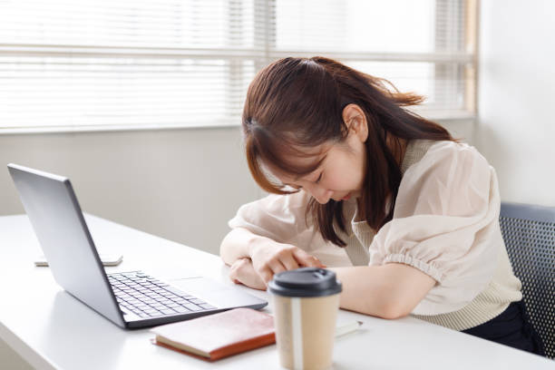 ある女性が机での仕事に疲れている。彼女の机の上にはパソコンと飲み物がある。 - うつ病  ストックフォトと画像