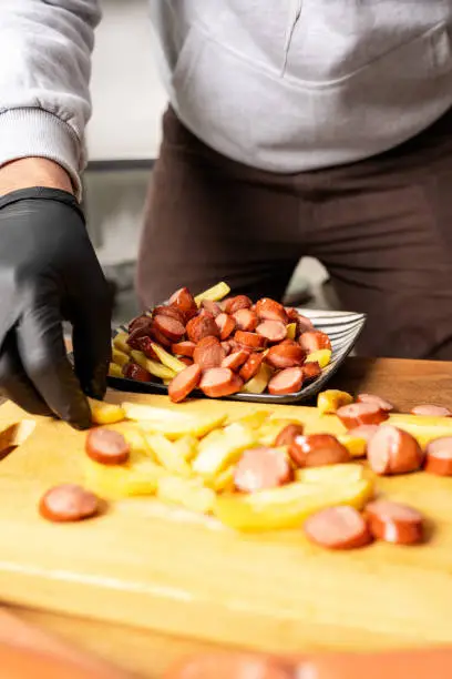 Photo of Vertical photo of a man mixing fries with sausages in a kitchen