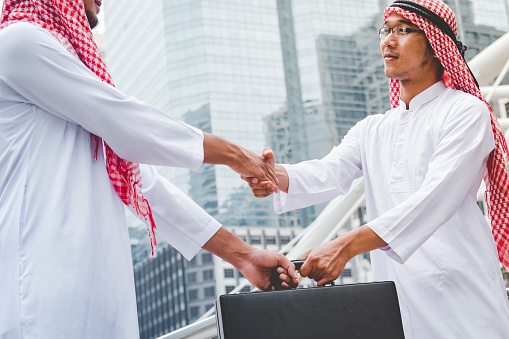 Arab Businessman shaking hands together. Teamwork business partner wear Muslim dress Shake Hands with Partnership Concept. Success UAE diversity people trust make commitment by handshake