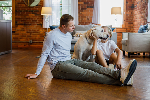 Full length shot of mid adult man, his nine year old son and their yellow Lab sitting on the living room floor, bonding and playing together.