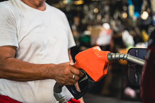 Worker holding a fuel injector is refueling a car in a gas station.