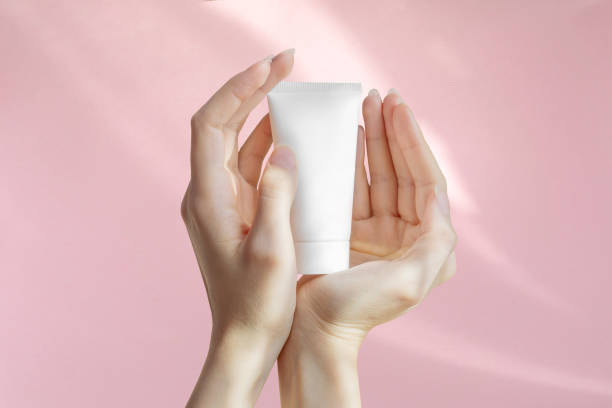 istock Woman's hands are holding an unmarked plastic container for cosmetics. White bottle for cream, toiletries on pink isolated background. Concept of skin care. Close-up, mockup style 1423529817