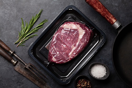 Vacuum packed beef steak. Ribeye steak and cooking utensils. Top view flat lay