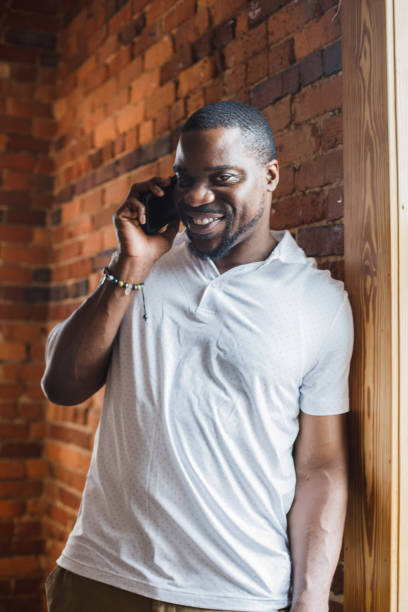 istock Charming Black man leaning against the wall, talking on the phone and smiling at camera 1423531986