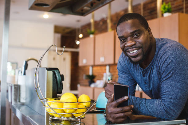 istock Man resting against the kitchen counter, using smart phone and smiling at camera 1423533185