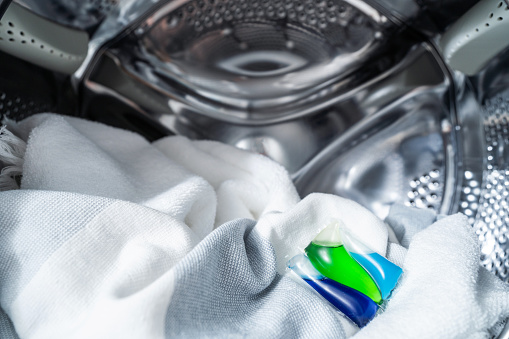 closeup of laundry gel capsule and textile clothes in metal drum of automatic washing machine, biodegradable cleaner