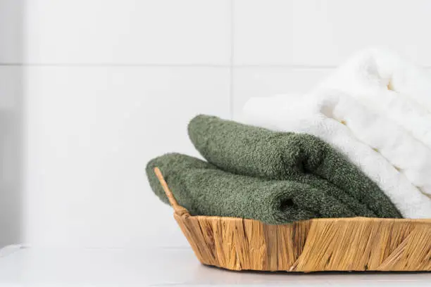 detail in interior design in modern bathroom, storage of fresh and clean bath towels tidy folded in wooden wicker basket on white background