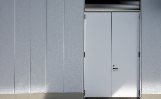 Close-up of white concrete wall with closed white metal door.