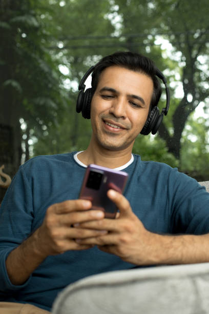 istock Man sitting in sofa with headphones using mobile phone 1423536729