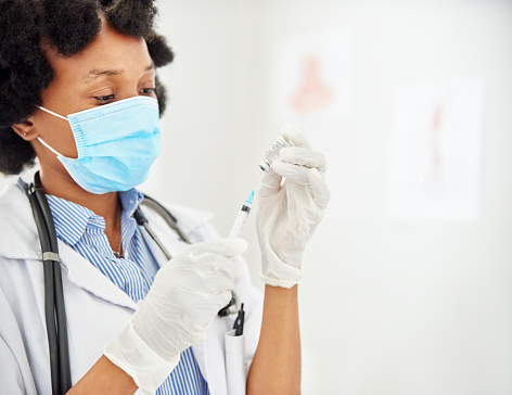 Close-up of a female doctor wearing face mask and rubber gloves filling a syringe with vaccine in clinic