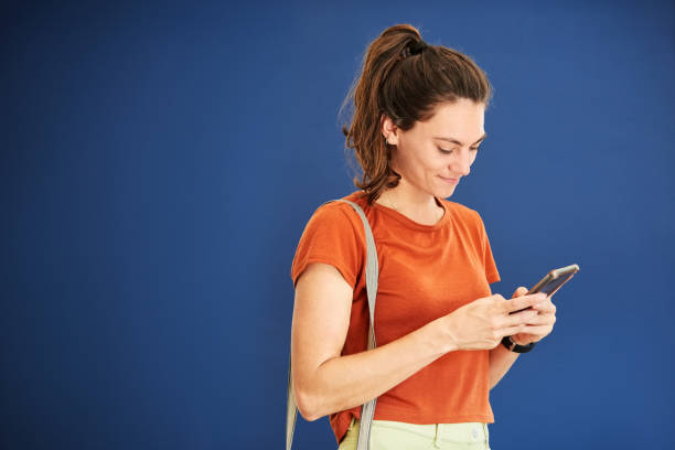 istock Young woman texting on her cell phone against blue background 1423539558